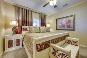 A bedroom with a bed, two bedside tables, a ceiling fan, a window with curtains, and a framed floral painting on the wall. - Pool & River Access! Luxury Hill Country Haven (New Braunfels)