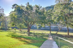 A park with a concrete pathway leading to a body of water, surrounded by trees and grassy areas. - Pool & River Access! Luxury Hill Country Haven (New Braunfels)
