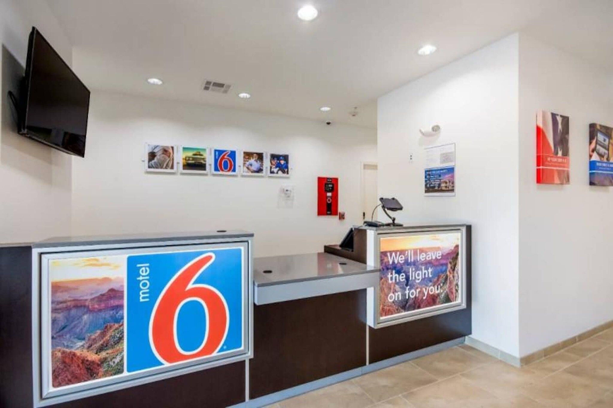 A motel reception desk with a large number '6' sign, a fire extinguisher, and a mounted television.