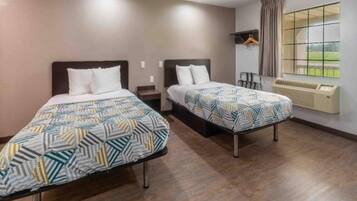 A hotel room with two beds, a window with a view, and a wall-mounted heater.