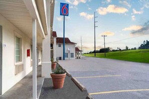 Un motel doté d’un parking, un bâtiment portant le numéro « 114 », et un panneau « 6 » indiquant le numéro du motel.