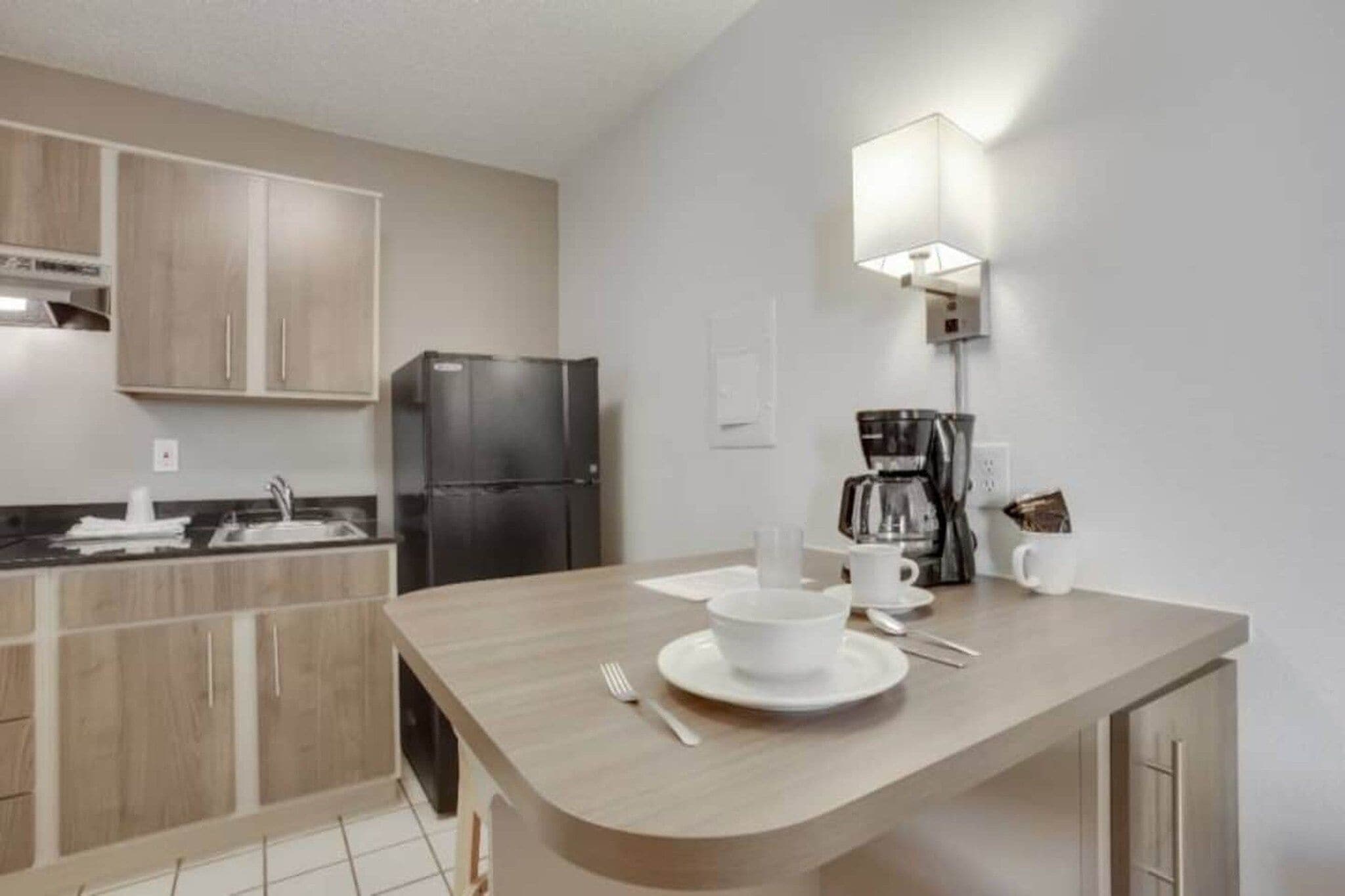 Una cocina moderna con refrigerador integrado, cafetera y comedor con mesa dispuesta para dos.