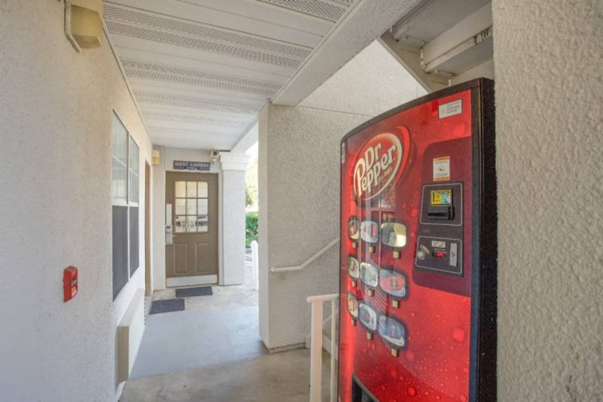 Máquina expendedora de Dr Pepper en un pasillo con una puerta y escalones que conducen a la entrada de un edificio.