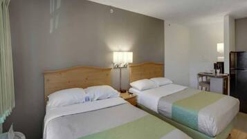 Una habitación de hotel con dos camas, un escritorio pequeño, un refrigerador y una mesita de noche con lámparas.