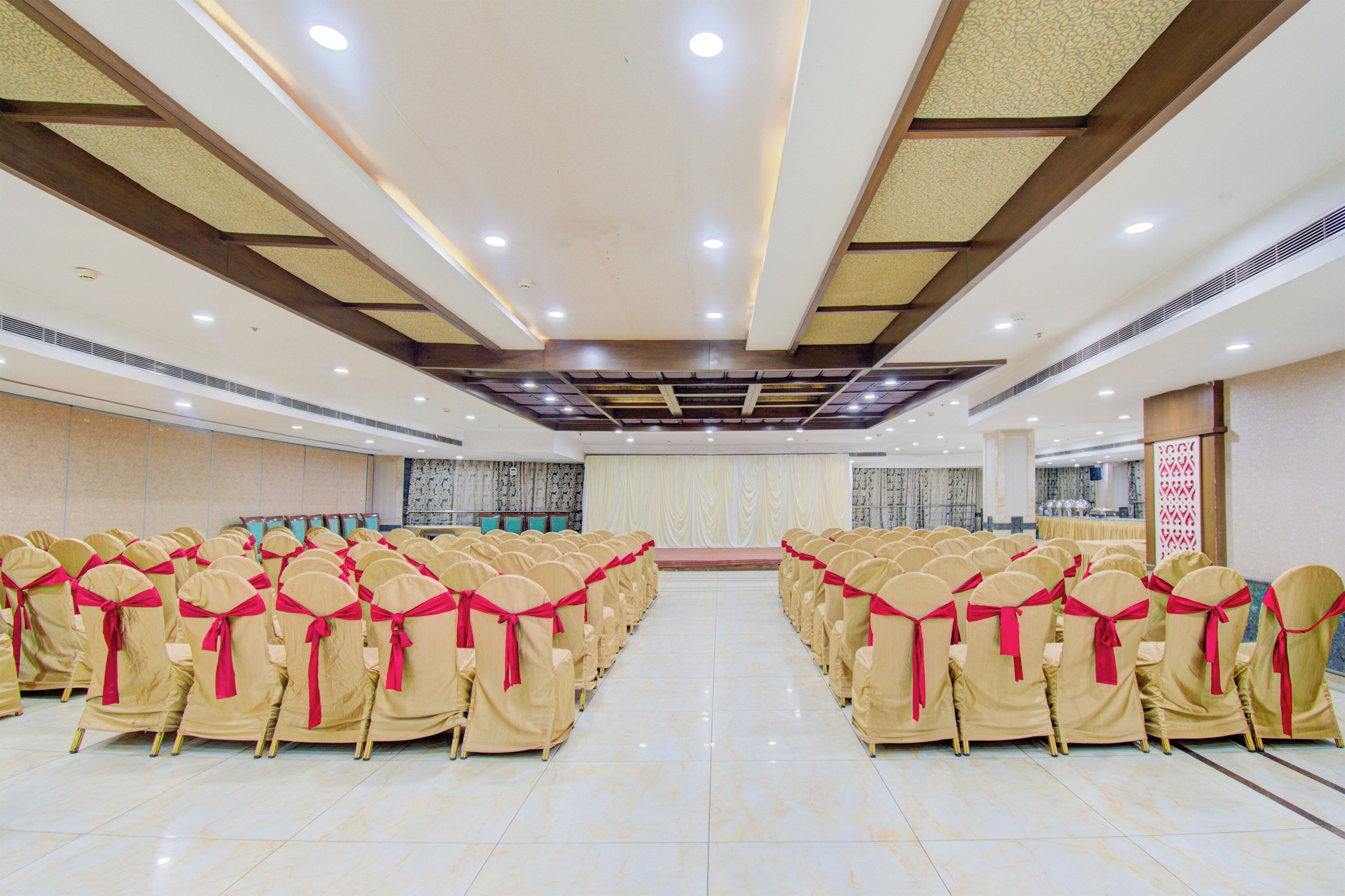 A conference room with rows of chairs, a stage, and a patterned ceiling.