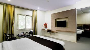 A hotel room with a large bed, a television mounted on the wall, a desk with a chair, and a window with curtains.