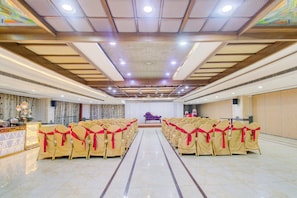 Un salón de banquetes con filas de sillas, un escenario e iluminación empotrada en el techo.