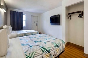 Ett hotellrum med två sängar, en tv som är monterad på väggen och ett fönster med gardiner.