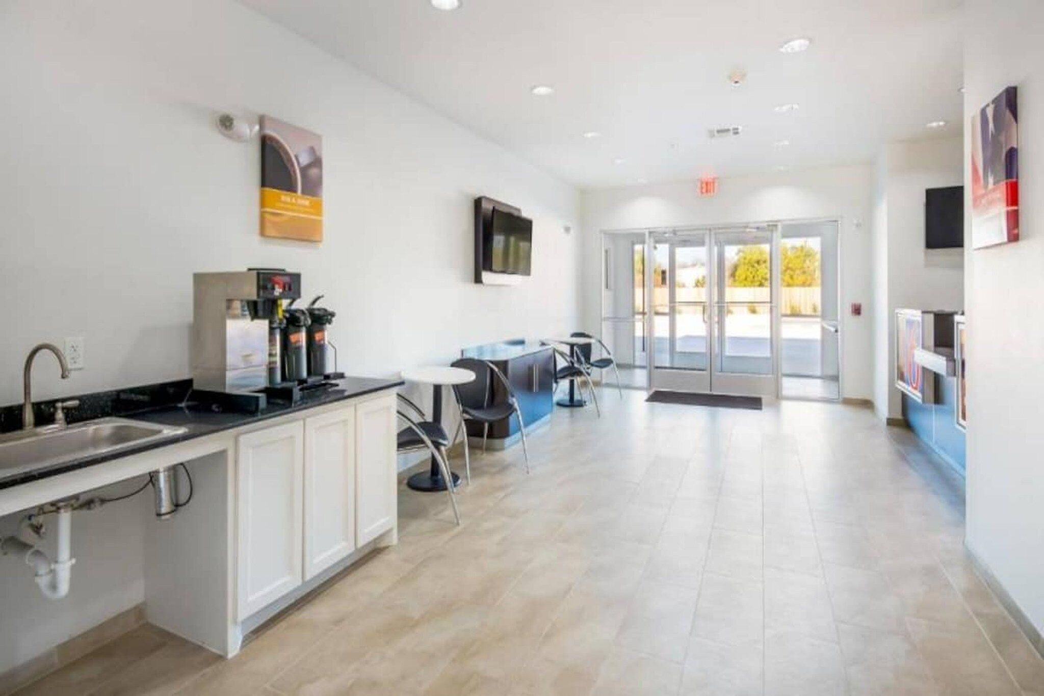 A modern kitchen with a sink, coffee machine, and cabinets. There is a seating area with tables and chairs.