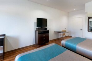 Ein Hotelzimmer mit zwei Betten, einem Fernseher auf einem Tisch, einem kleinen Tisch und einer Tür.