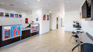 A hotel reception area with a counter, a digital display, and a seating area with tables and chairs.
