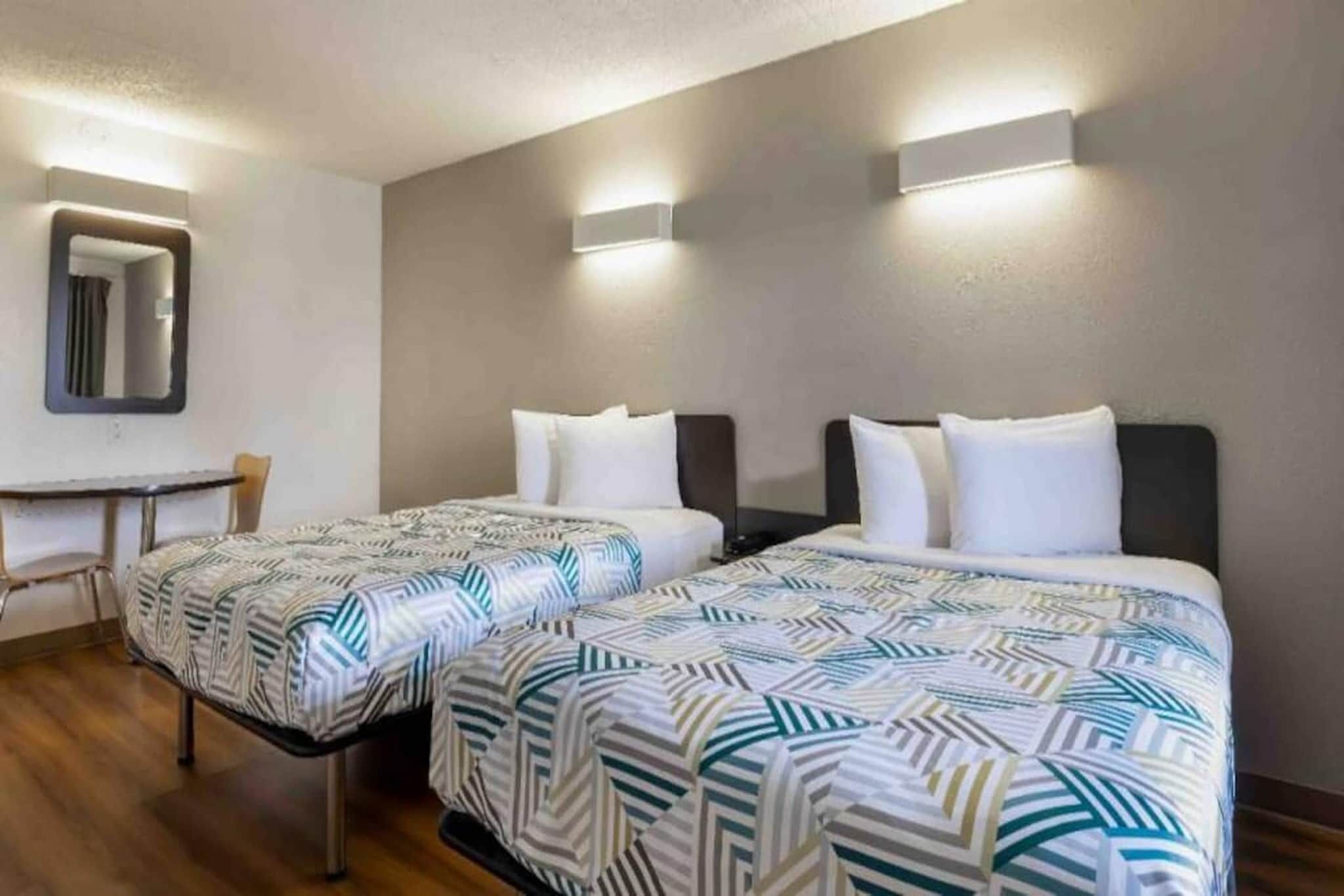 A hotel room with two beds, a desk, and a mirror.