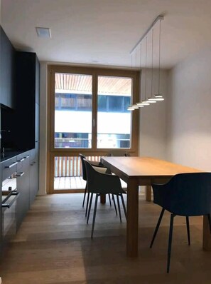 A modern kitchen with a dining table and chairs, a TV, and a large window with a view. - Central 2.5-Room Apartment in Flims - Ski-in/ski-out (Flims)