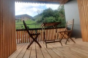 A wooden deck with two chairs and a small table, overlooking a grassy area with trees and a distant building. - Central 2.5-Room Apartment in Flims - Ski-in/ski-out (Flims)