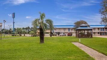 A hotel with a blue roof, a covered outdoor seating area, and a well-maintained lawn.