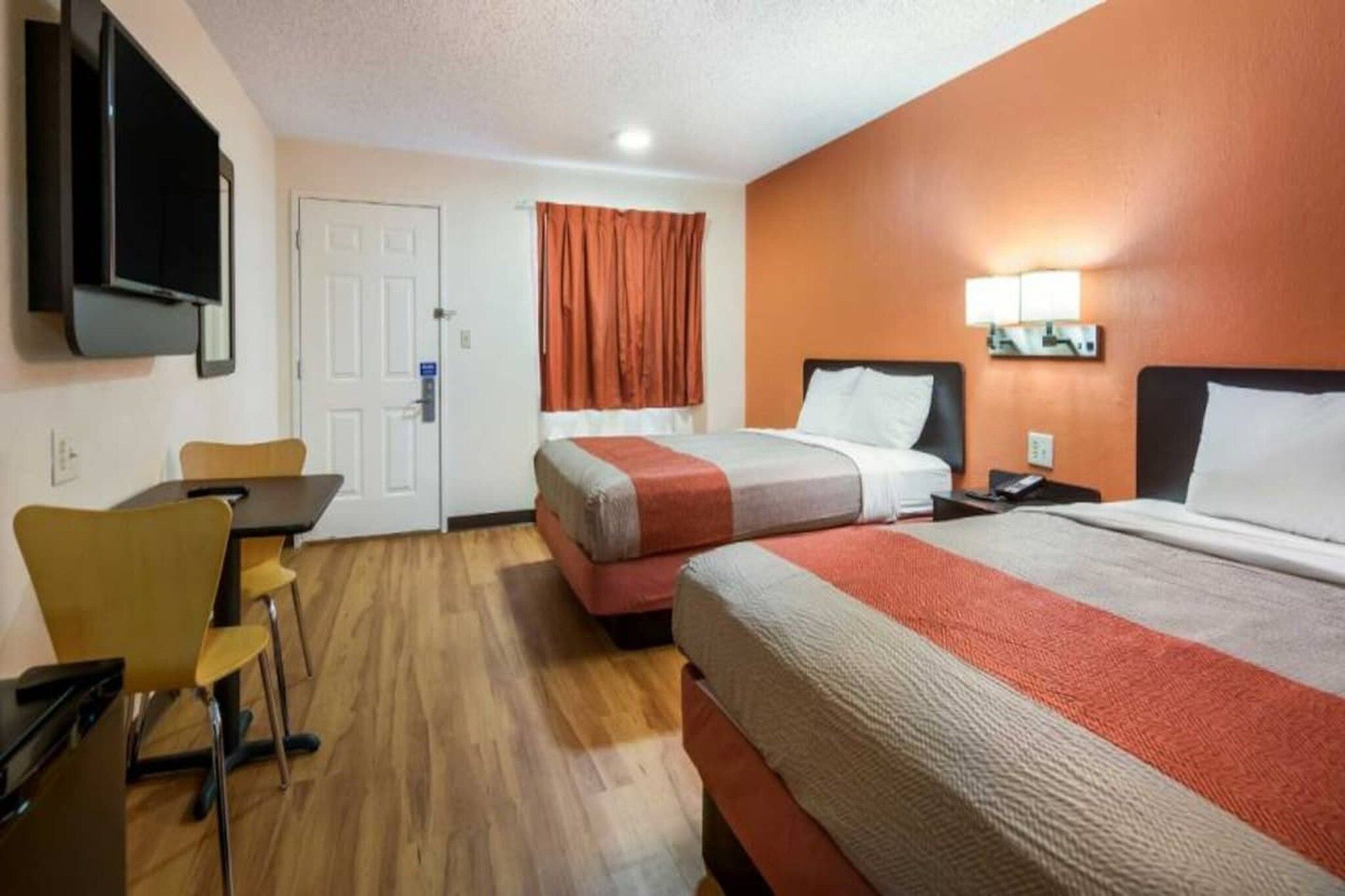 A hotel room with two beds, a desk, a chair, a TV, and a door.
