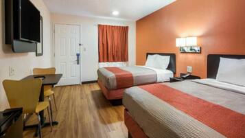 A hotel room with two beds, a desk, a chair, a TV, and a door.