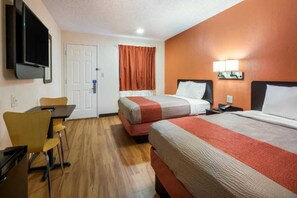 Ein Hotelzimmer mit zwei Betten, einem Schreibtisch, einem Sessel, einem Fernseher und einer Tür.