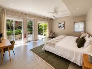 A spacious bedroom with a large bed, a ceiling fan, and a view of a garden through glass doors. - EDBAY - Edwards Beach Retreat | Steps To Balmoral (Mosman)