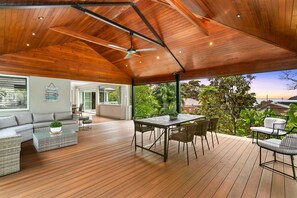 An open-plan living area with a wooden ceiling, a sofa set, a dining table with chairs, and a view of greenery outside. - EDBAY - Edwards Beach Retreat | Steps To Balmoral (Mosman)