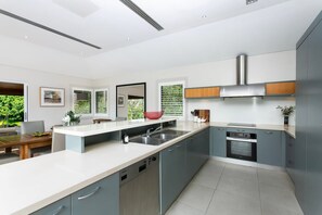 A modern kitchen with a central island, built-in appliances, and a view of greenery outside. - EDBAY - Edwards Beach Retreat | Steps To Balmoral (Mosman)