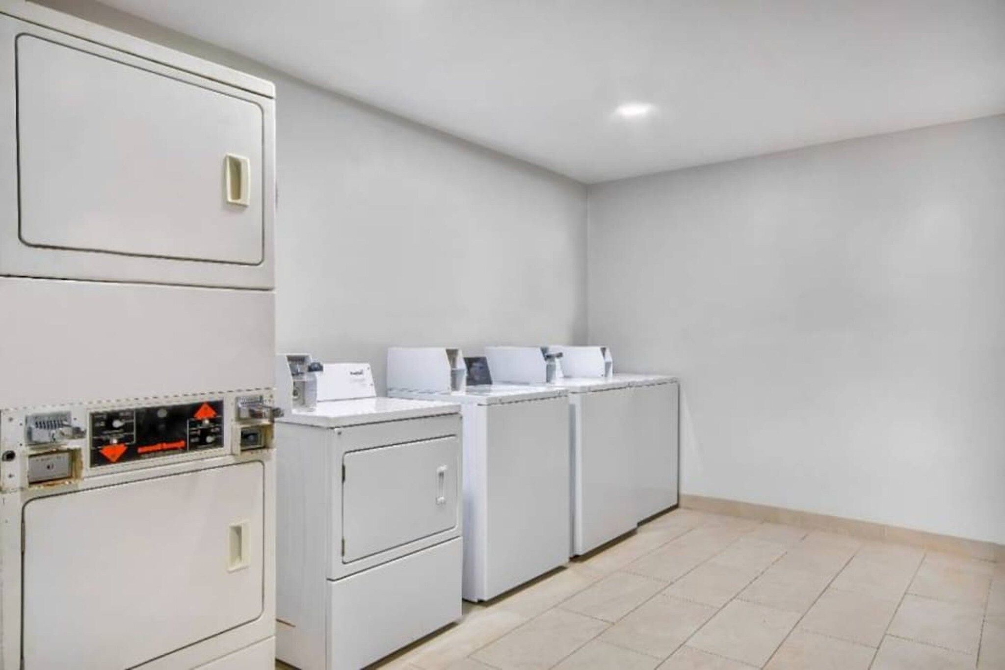 A laundry facility with stacked washing machines and dryers, a control panel, and a tiled floor.