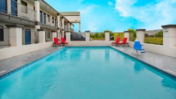 A swimming pool with red lounge chairs and a clear blue sky.