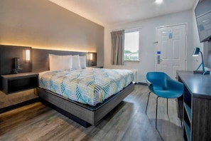 Una habitación de hotel con cama, mesita de noche, escritorio, silla y ventana con cortinas.