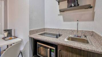 A compact kitchenette with a microwave, a sink, and a stovetop.