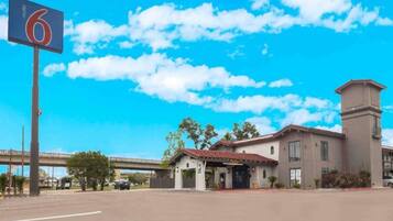 A motel with a clear blue sky, a parking lot, and a building with a red-tiled roof.