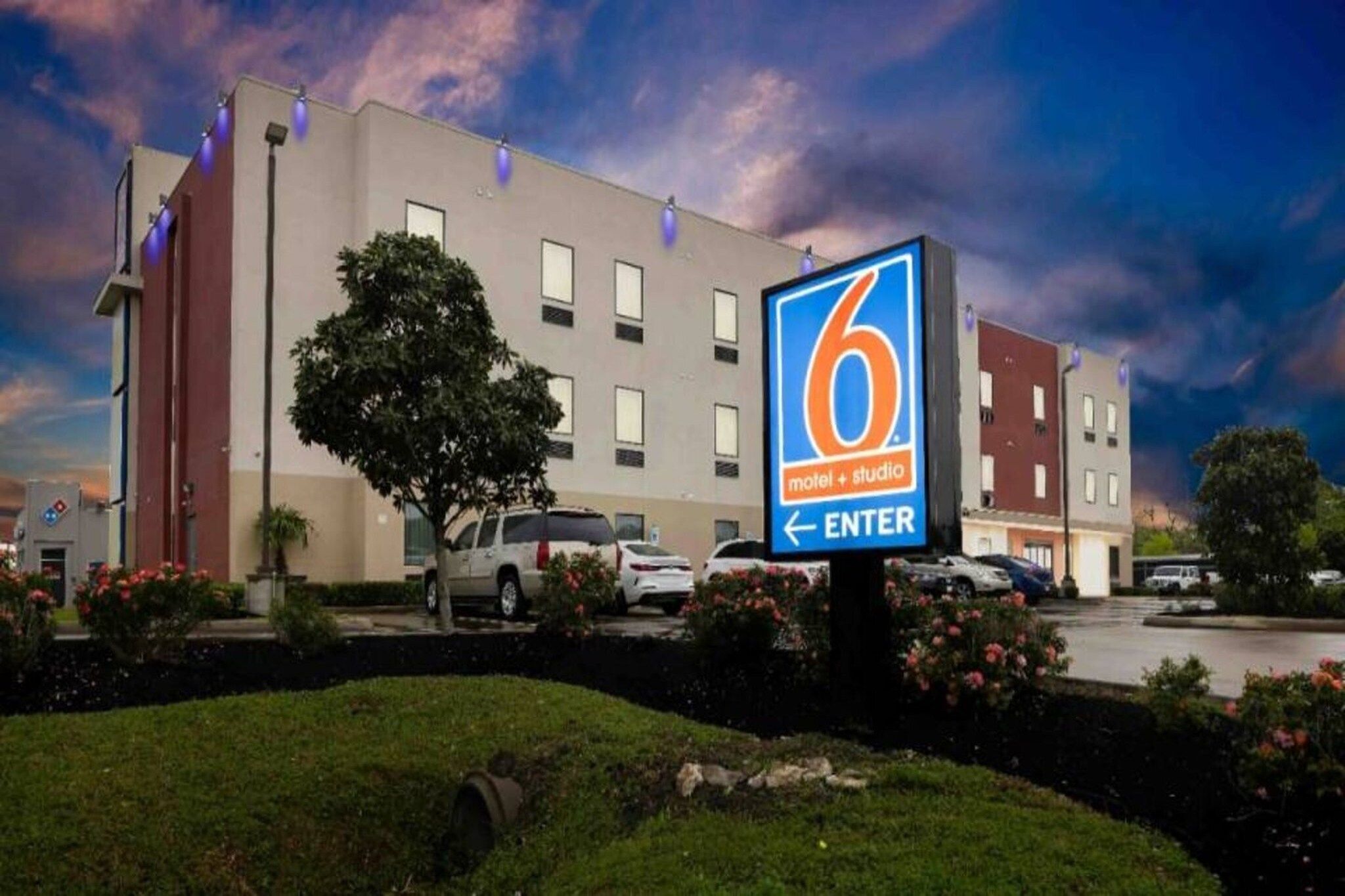 Un hôtel de type motel et studio, doté d’une enseigne d’entrée bien visible, d’un espace de stationnement et d’un bâtiment avec de nombreuses fenêtres.