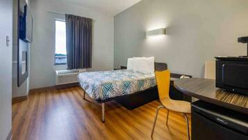A hotel room with a bed, a desk, a chair, a television, and a window with curtains.