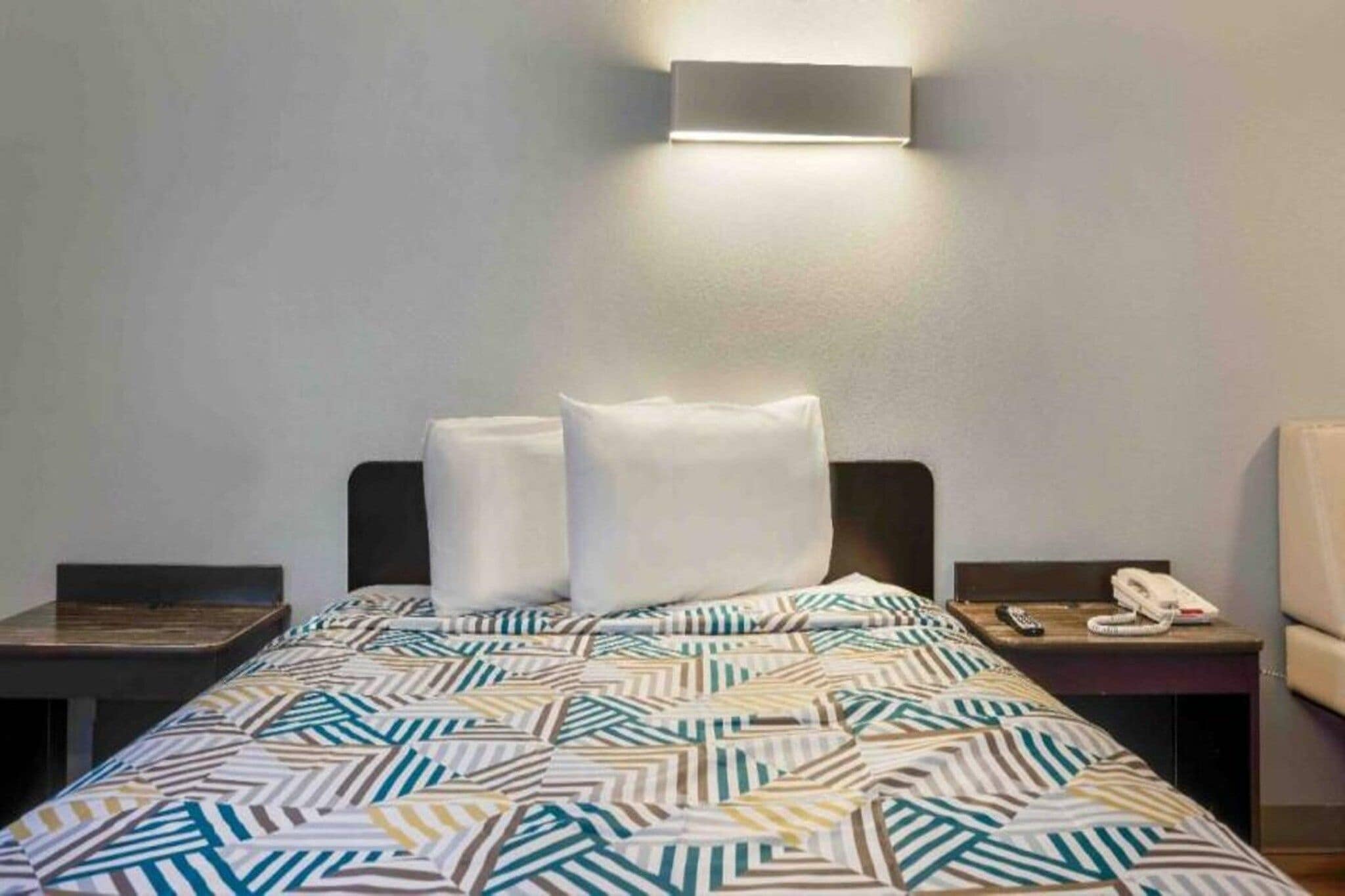 Une chambre d’hôtel comprenant un lit, deux tables de chevet, une lampe fixée au mur et un téléphone.