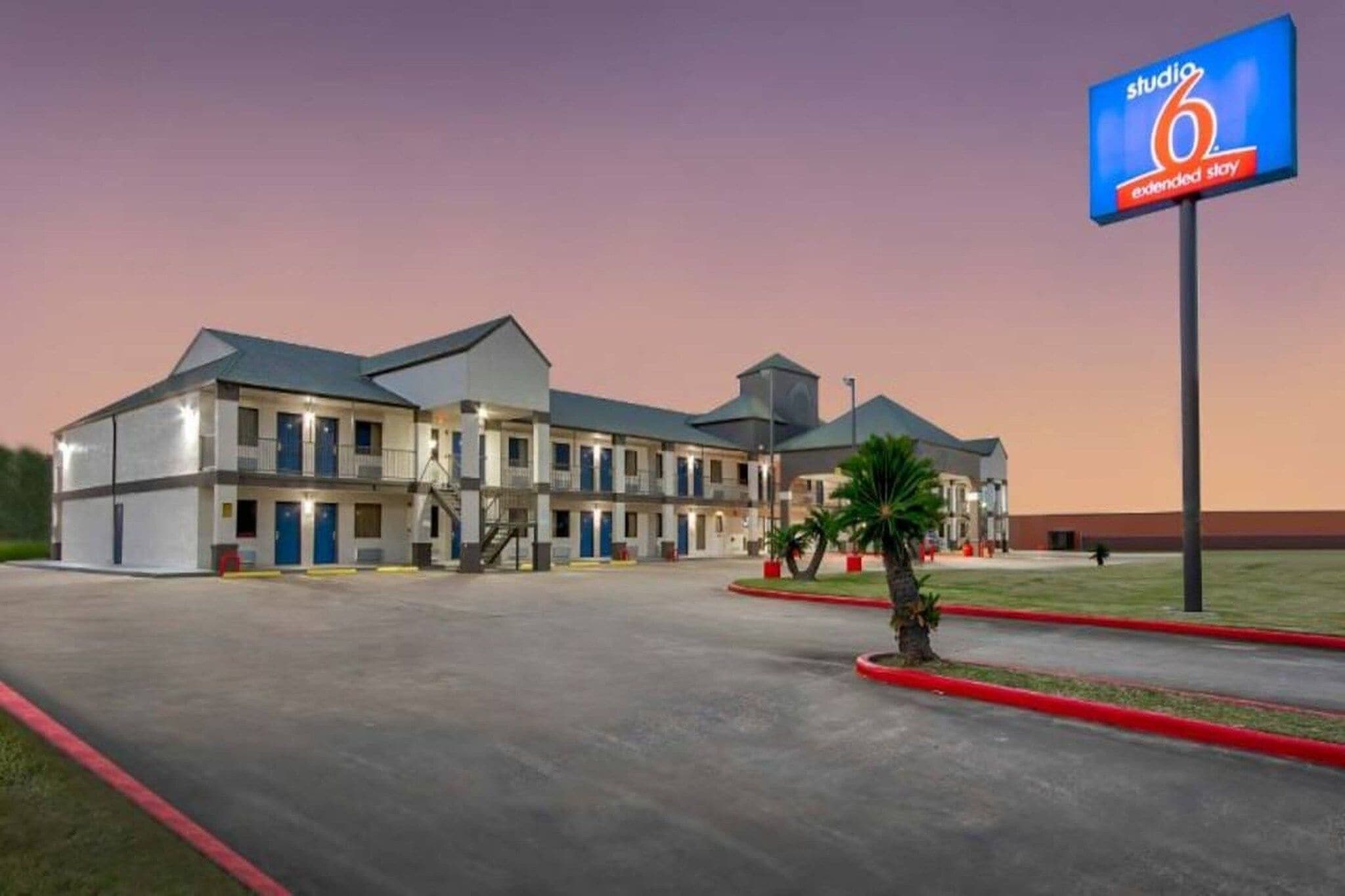Un motel à plusieurs étages, doté d’un toit plat, d’une entrée centrale et d’un parking.