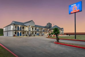 Een motel met meerdere verdiepingen, een plat dak, een centrale ingang en een parkeerplaats.