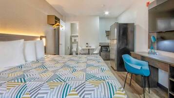 Une chambre d’hôtel comprenant un lit, un bureau, une chaise, une kitchenette et une salle de bain.