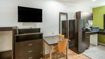 Een compacte kitchenette met een koelkast, magnetron en een klein eettafeltje met een stoel.