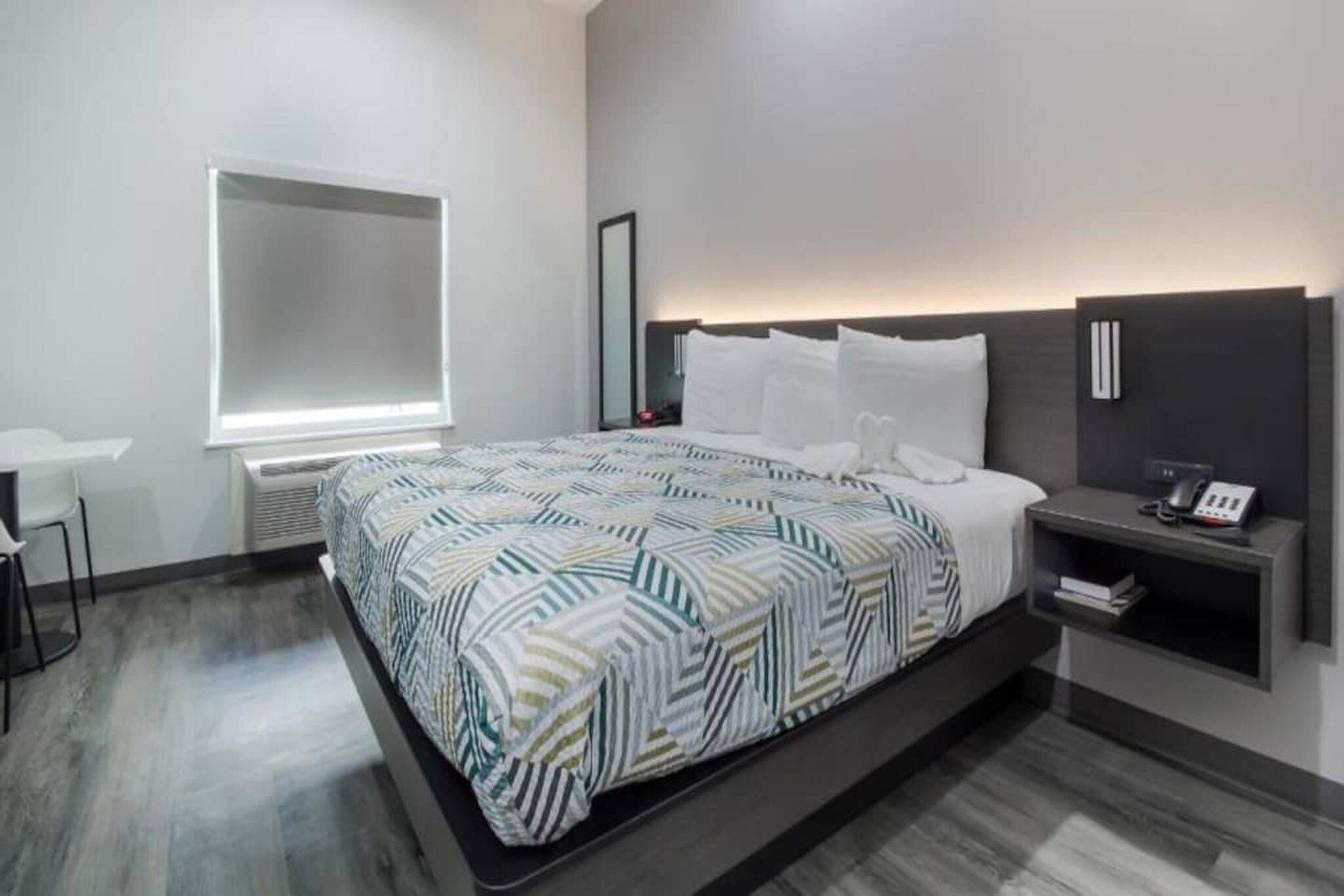 A modern hotel room with a large bed, bedside tables, a bedside lamp, and a window.