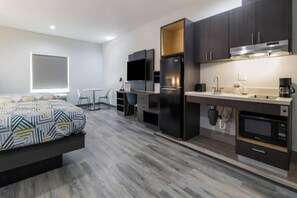 A modern hotel room with a bed, a desk, a flat-screen TV, a refrigerator, a microwave, a coffee maker, and a window. - 1 King Bed | Non-Smoking, Kitchen (Katy)