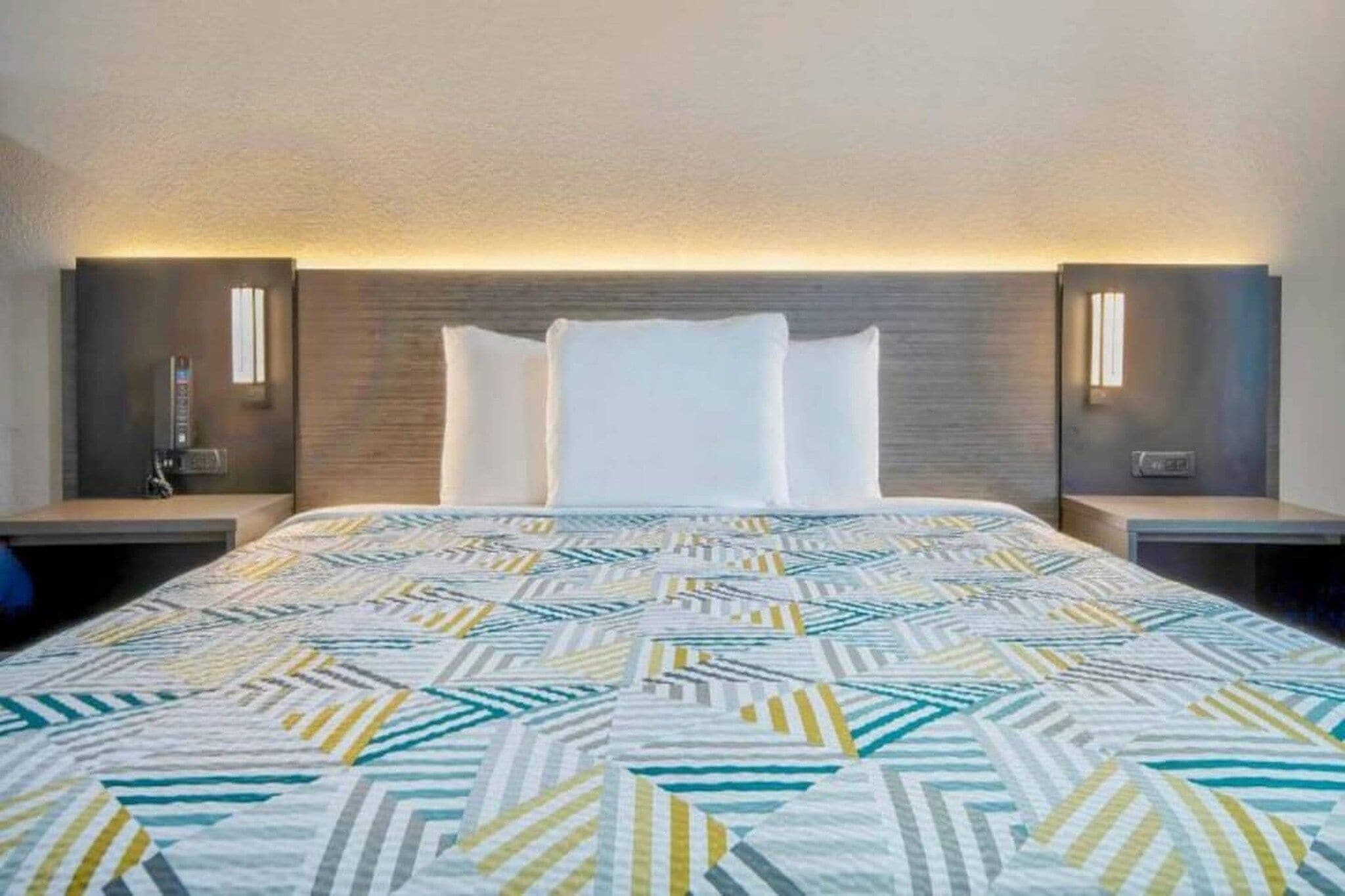 Une chambre d’hôtel avec un lit, deux tables de chevet et des lampes fixées au mur.