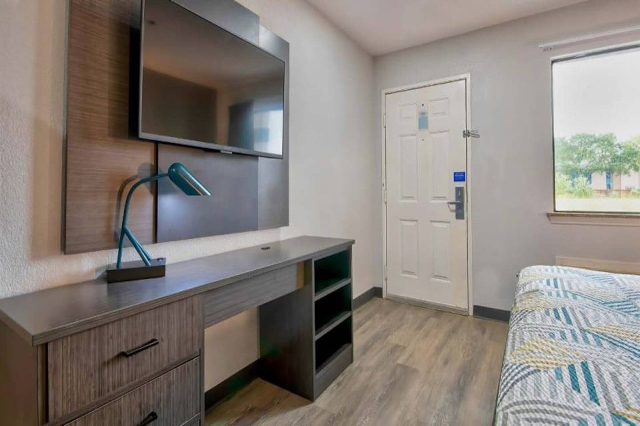 A bedroom with a bed, a desk with a lamp, a wardrobe, and a door.