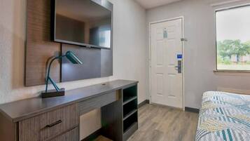 A bedroom with a bed, a desk with a lamp, a wardrobe, and a door.