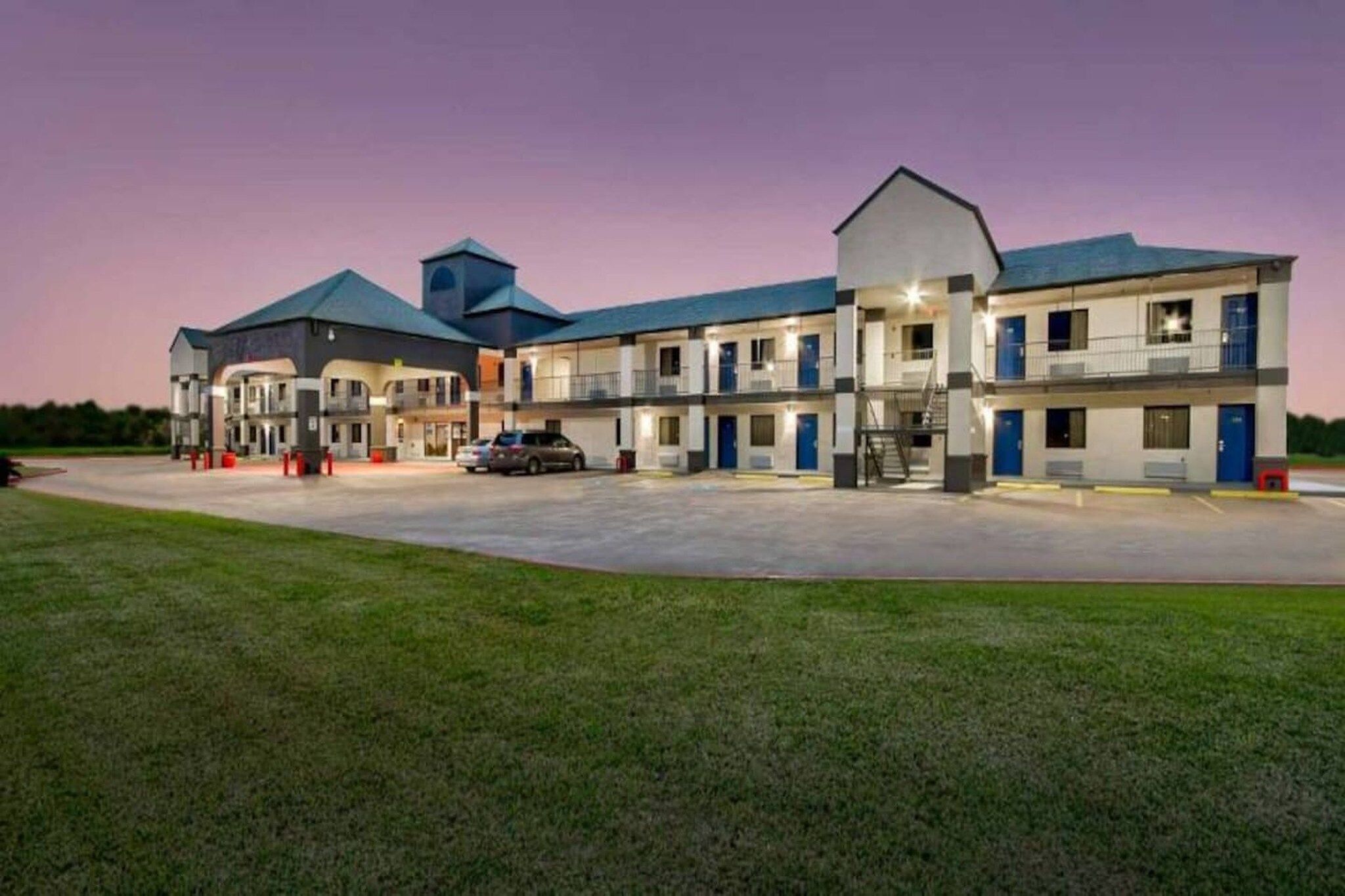 A motel with multiple rooms, a parking lot, and a grassy area in front.