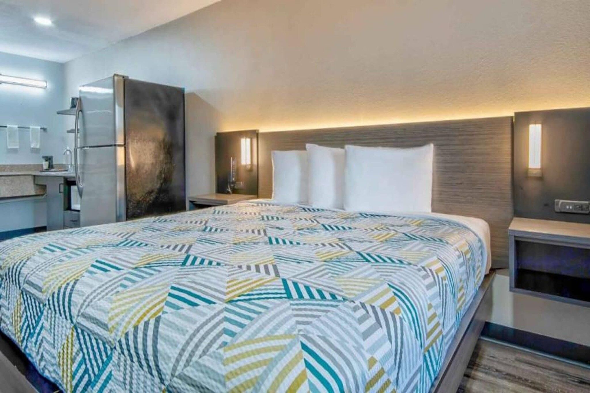 A hotel room with a large bed, a nightstand, a dresser, and a modern bathroom.