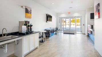 A modern kitchen with a sink, coffee machine, and cabinets. There is a seating area with tables and chairs.