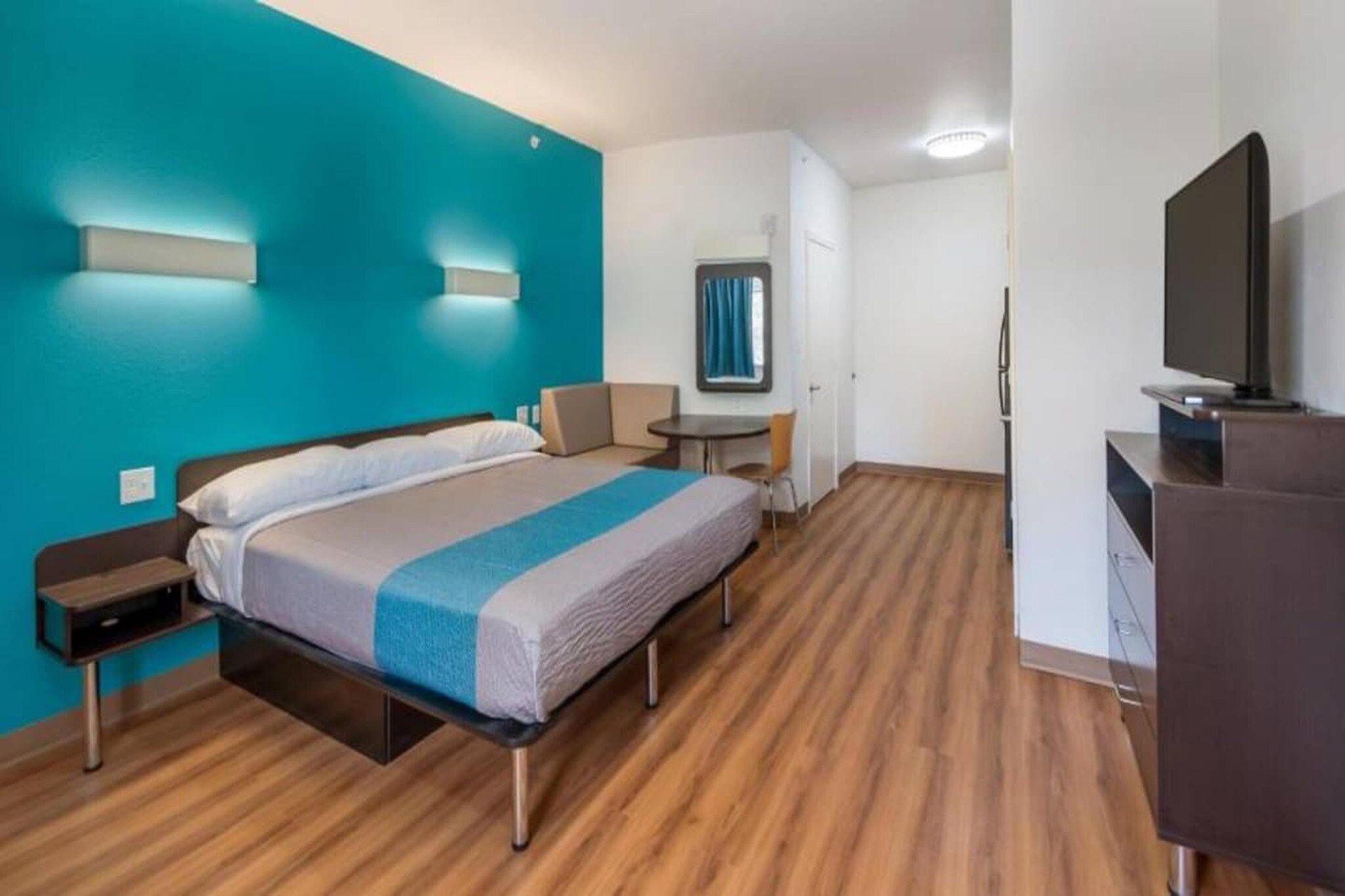 A hotel room with a bed, bedside table, a desk with a chair, a television, and a mirror on the wall.