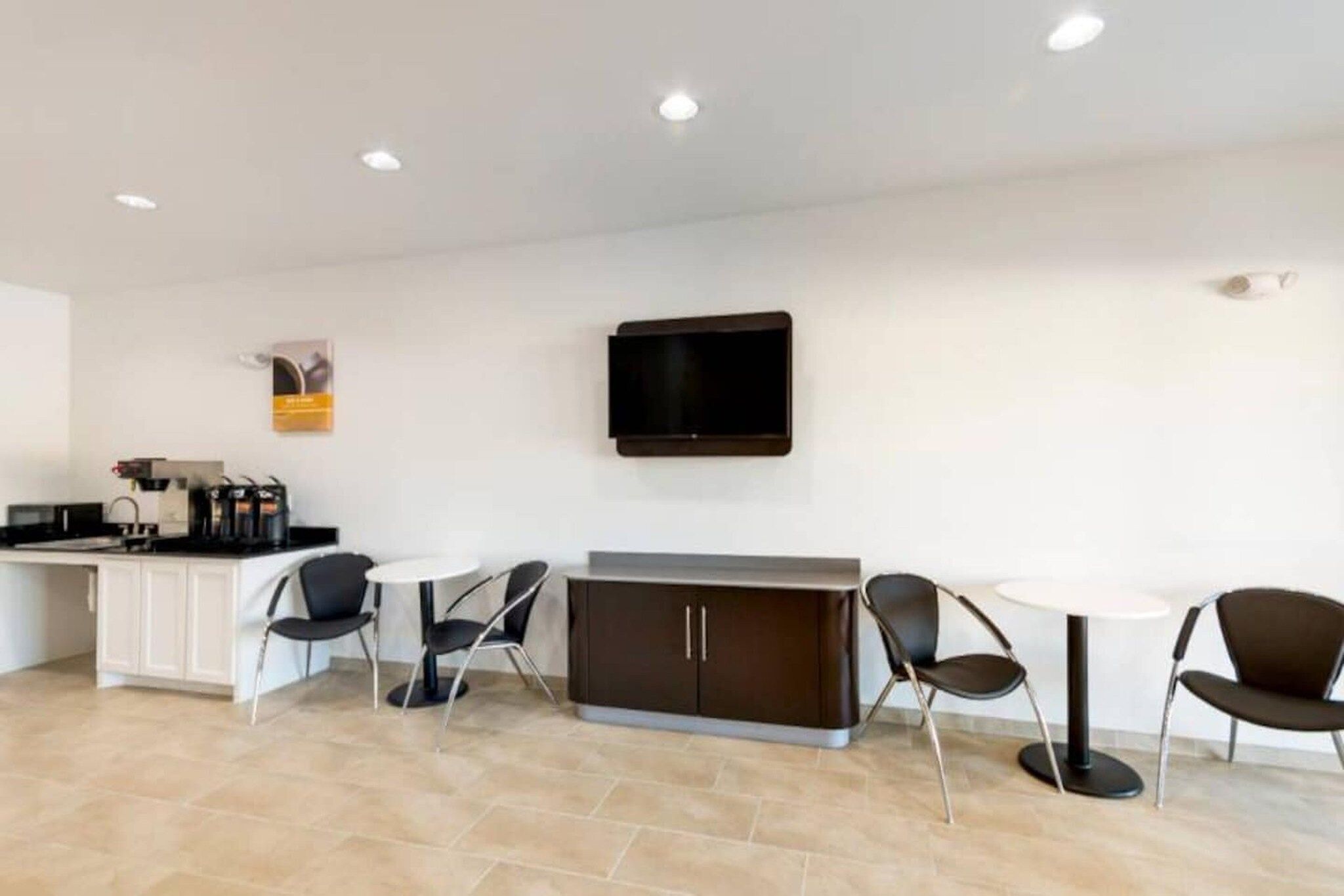 A modern hotel room with a kitchenette, a flat-screen TV mounted on the wall, and a seating area with a table and chairs.
