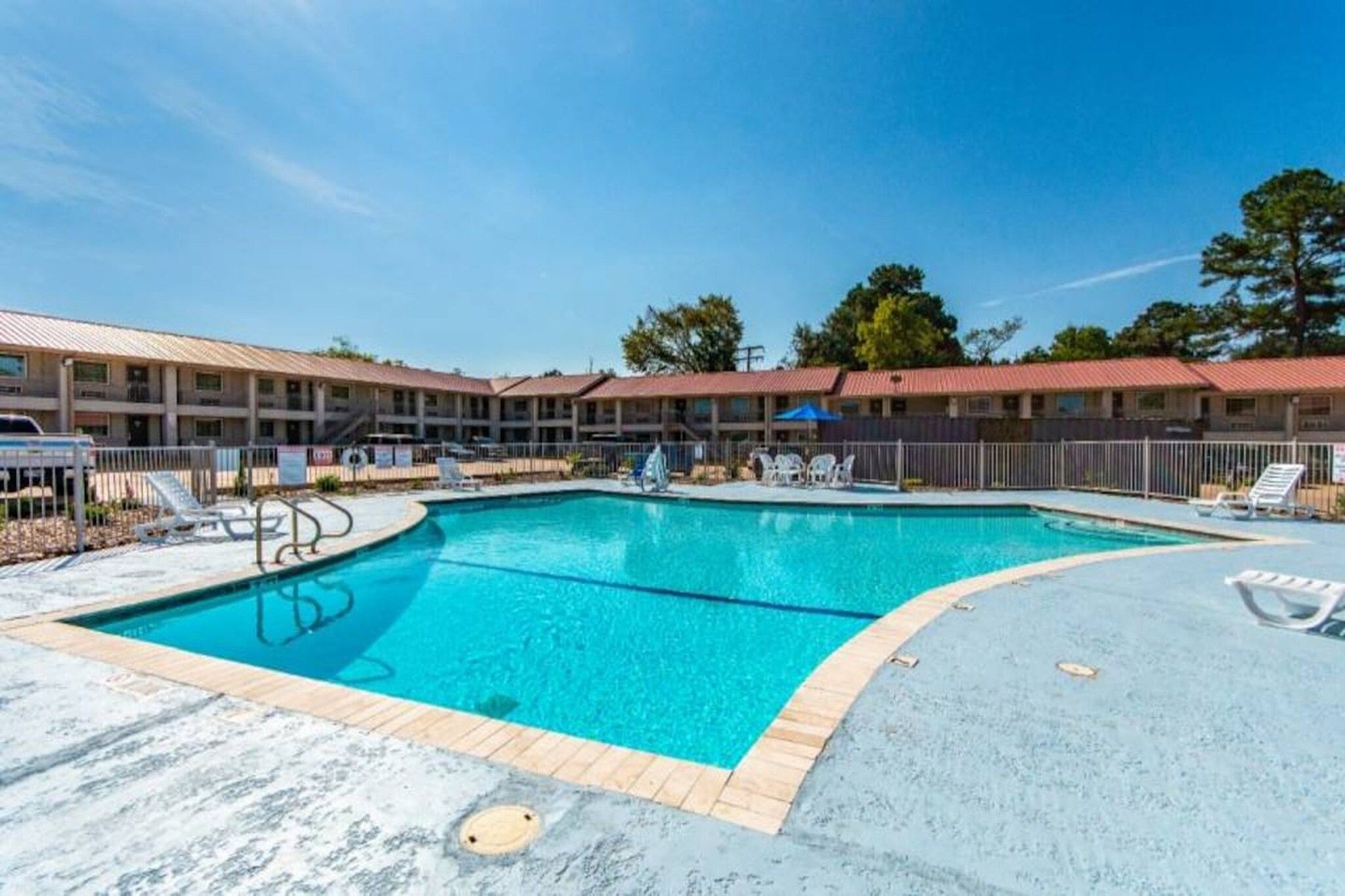 En swimmingpool med solstolar och en byggnad med ett rött tak i bakgrunden.