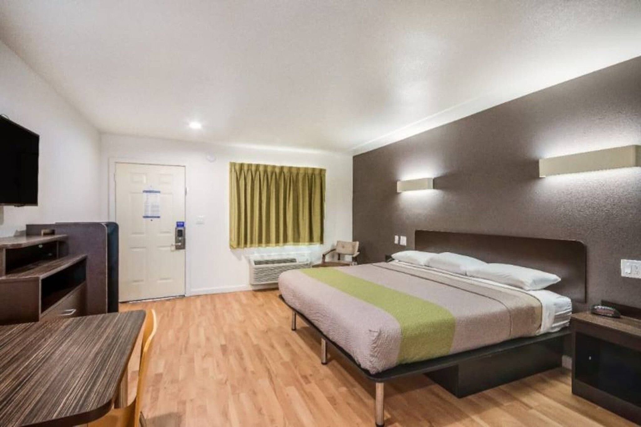 A hotel room with a bed, bedside table, and a desk with a chair.