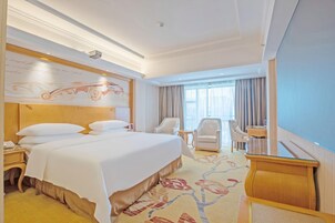 Habitación de hotel con una cama grande, dos sillones, un escritorio y vistas al exterior.